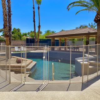 A backyard pool with a safety fence surrounded by palm trees under a clear blue sky.