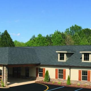 A commercial building with a dark roof and surrounded by greenery under a clear blue sky.