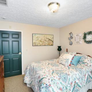 A cozy bedroom with patterned bedding, wall decor, and a dresser next to a dark door.