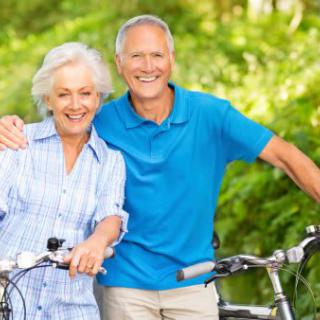 An elderly couple enjoying a bike ride outdoors in a lush, green setting.