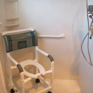A bathroom with a shower area equipped with a shower chair and grab bar for accessibility.