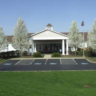 A front view of a building with a white entrance, surrounded by blooming trees and a parking lot.