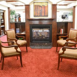 A cozy seating area with four chairs arranged around a fireplace, featuring bookshelves and a painting on the wall.