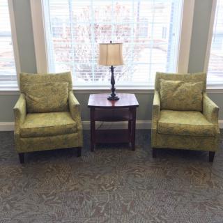 A cozy seating area with two green chairs and a lamp on a side table by the window.