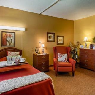 A cozy bedroom with warm lighting, featuring a bed, armchair, and decorative artwork.