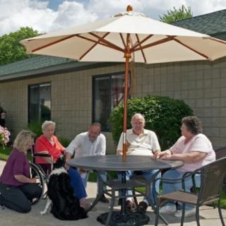 A group of people sitting around a patio table with an umbrella, enjoying a sunny day.