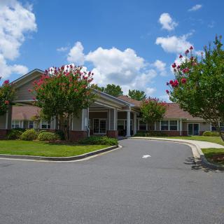 A view of a building entrance surrounded by greenery under a blue sky with clouds.