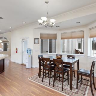A spacious kitchen and dining area with hardwood floors, featuring a large table set beneath a chandelier, surrounded by windows allowing ample natural light.