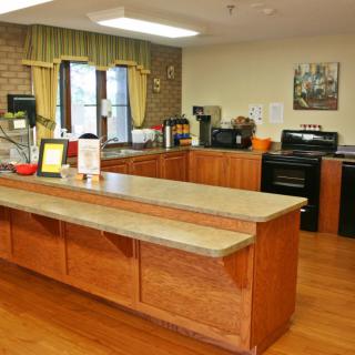 A kitchen interior with wooden cabinets and flooring, featuring a large central countertop and various appliances.