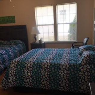 A cozy bedroom featuring two beds with patterned bedding, a lamp, and a window allowing natural light.
