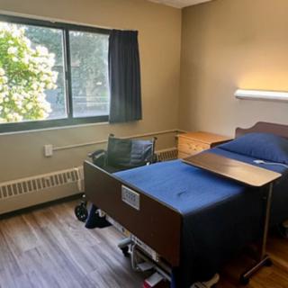 A clean hospital room featuring a bed, window with curtains, and a small desk.