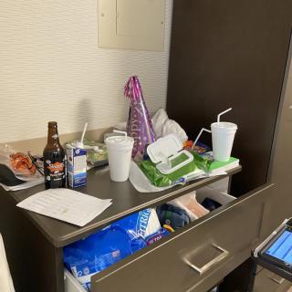 A cluttered bedside table in a hospital room with drinks and personal items.