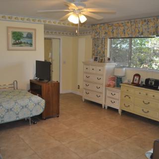 A cozy bedroom with a bed, dresser, and ceiling fan, featuring a large window and decorative elements.
