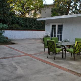 A serene backyard patio with a green-themed outdoor dining set surrounded by lush greenery.