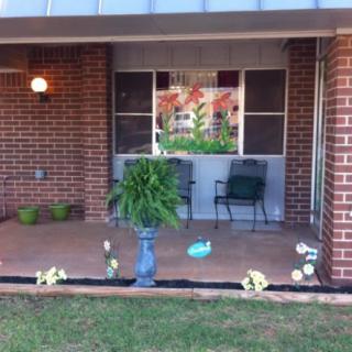 A cozy porch with chairs and plants in front of a brick house.