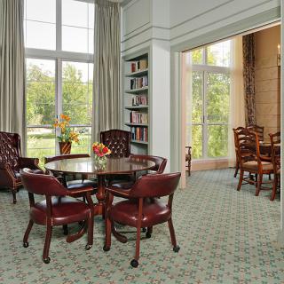 A cozy living and dining area with elegant furniture, bookshelves, and large windows.