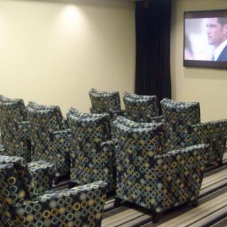 A cozy home theater setup with patterned armchairs facing a wall-mounted television.