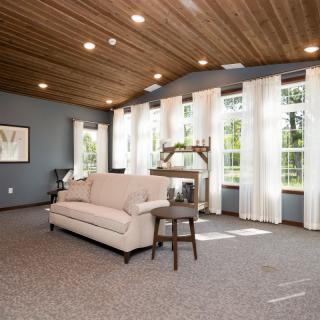 A spacious living room with large windows, a cozy sofa, and a wooden ceiling allowing ample natural light.