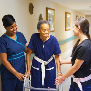 Caregivers assisting an elderly woman with mobility in a healthcare setting.