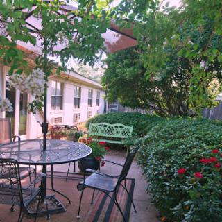 A serene outdoor garden space featuring a table with chairs, surrounded by lush greenery and vibrant flowers.