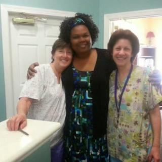 A group of three women smiling together in a healthcare setting.