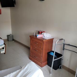 A simple hospital room featuring a bed, a nightstand, a walker, and a trash can.