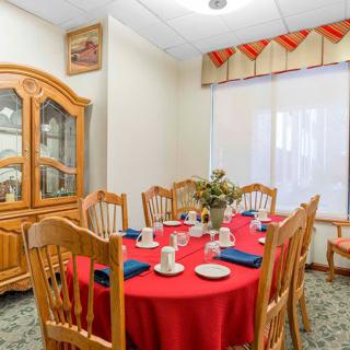 A cozy dining room with a round table set for tea, featuring a red tablecloth and wooden chairs.