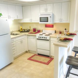 A cozy kitchen with white cabinets, featuring modern appliances and a small breakfast bar.