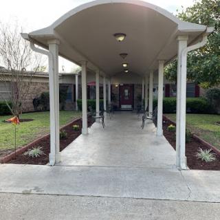 A serene walkway leading to a building, flanked by benches and landscaped greenery.