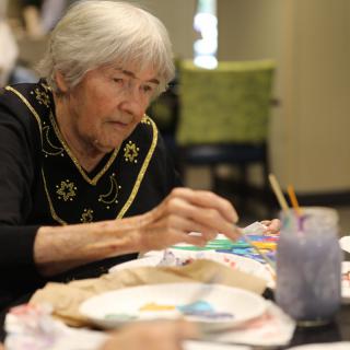 An elderly woman engaged in a painting activity indoors.