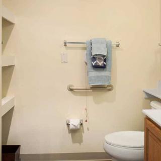A bathroom featuring a toilet, sink, towel rack, and shelves.