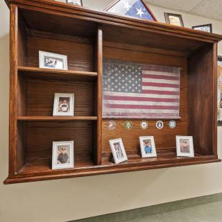 A wooden display case featuring an American flag, photographs, and military medals.