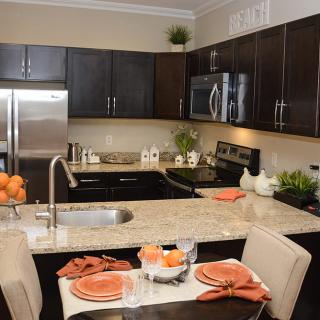 A modern kitchen with stainless steel appliances and a granite countertop, featuring a small dining area with orange-themed decor.
