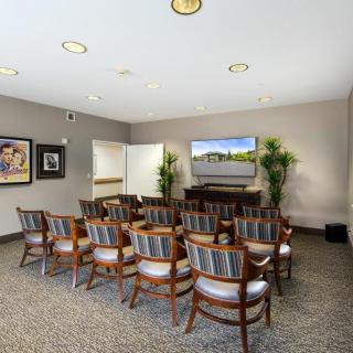 A neatly arranged conference room with rows of chairs facing a projection screen, complemented by decorative plants and framed artwork on the walls.