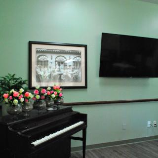 A cozy living space featuring a piano with colorful flowers, a framed artwork on a green wall, and a mounted television.