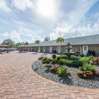 A sunny view of a well-landscaped motel with a brick pathway and palm trees.