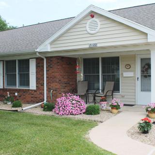 A charming house with a well-maintained front yard and garden, featuring flower pots and patio chairs on the porch.