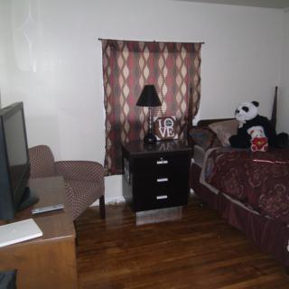 A cozy bedroom with a bed, nightstand, TV, and a panda plush toy sitting on the bed.