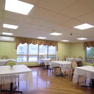 A spacious dining area featuring neatly arranged tables and chairs, illuminated by soft overhead lighting.