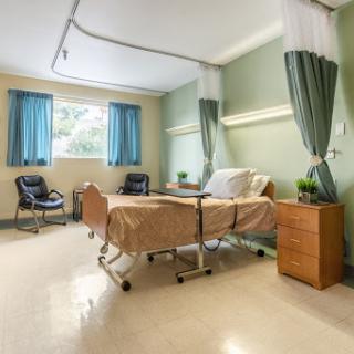 A well-lit and organized hospital patient room, featuring a bed, window with curtains, and comfortable seating.