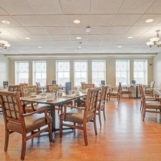 A spacious and well-lit dining room with neatly arranged tables and chairs, featuring large windows and wooden flooring.