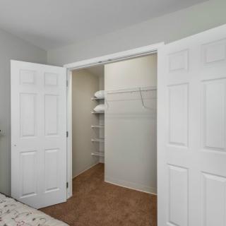 A bedroom closet with open white doors and built-in shelves.