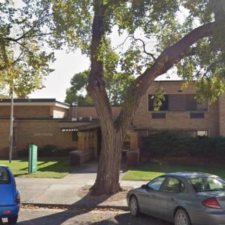 A suburban building with cars parked under a large tree on a sunny day.