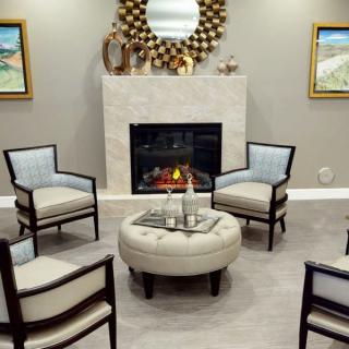 A modern living room with upholstered chairs arranged around a round ottoman, featuring a fireplace and stylish mirror above it.
