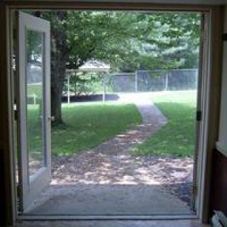 View of a backyard through an open door with a pathway leading to the garden.