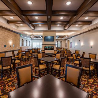 An empty dining area with neatly arranged tables and chairs, featuring elegant lighting and decorative ceiling beams.