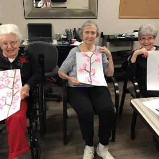 A group of elderly individuals proudly display their artwork during a painting activity.