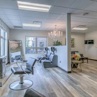 A modern and well-lit hair salon with stylish chairs and a chandelier.