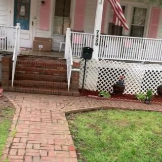 A charming house with a brick walkway leading to a front porch adorned with railings and an American flag.