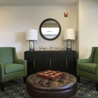 A cozy living room setup with green chairs, a round coffee table, and a mirror above a sideboard flanked by lamps.